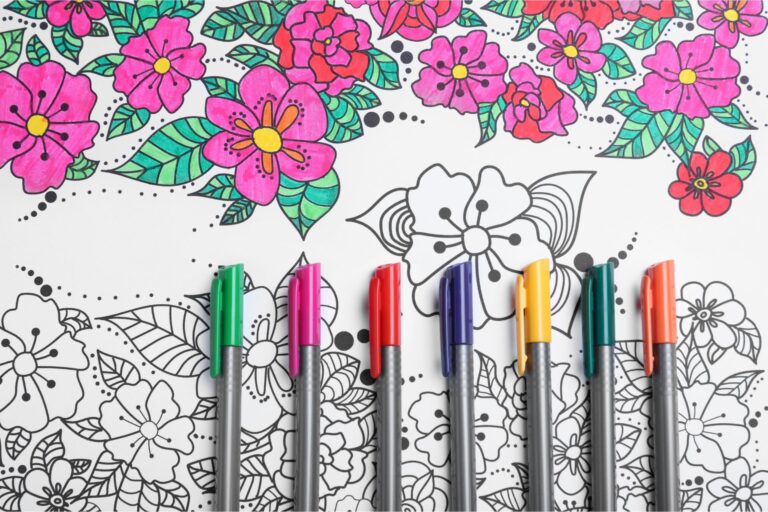 coloring page with pink flowers and green leaves with markers laying on top of page